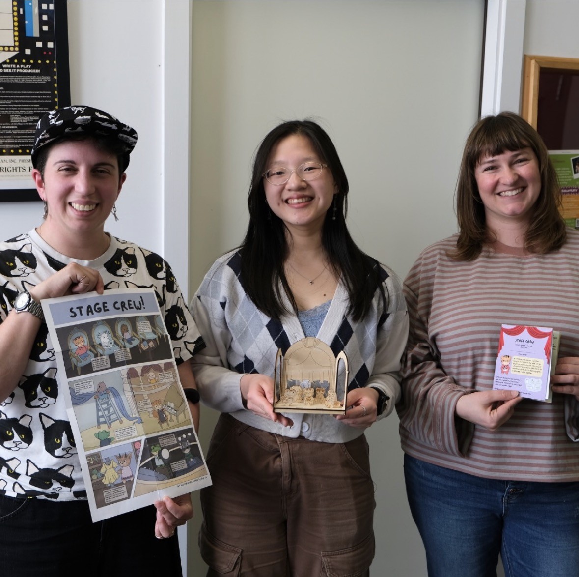 From left to right: Madeline holding the poster side of the leaflet, Diyu holding the puzzle stage with characters, and Ali holding the activity book, closed.